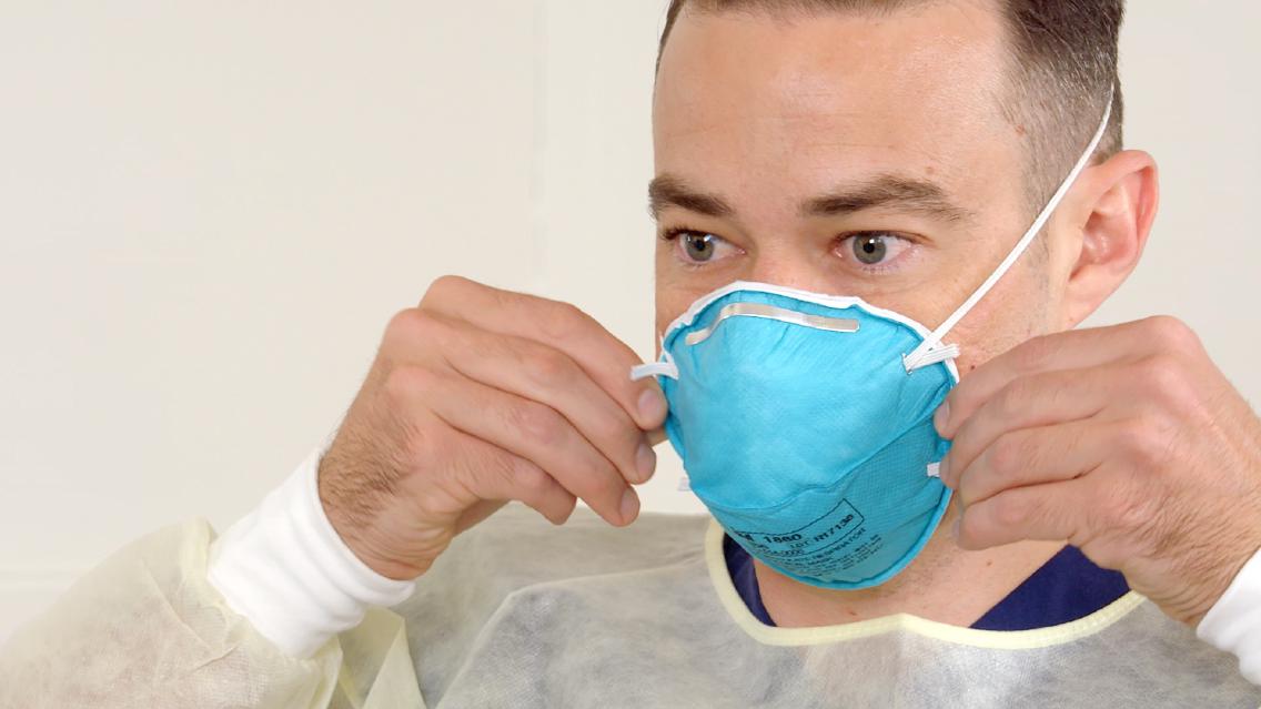 A man in personal protective equipment adjusts his mask